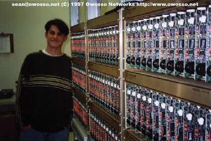 Sean Heiney standing beside a wall of rack-mounted modems at the ShiaNet modem bank, 1997